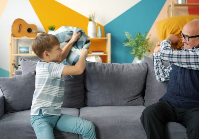 Grandfather old man is playing with joyful kid fighting pillows having fun in apartment enjoying game together. Lifestyle, people and happy family concept.